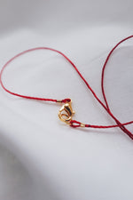 Gold fish pendant on a red string necklace, symbolizing luck and abundance.