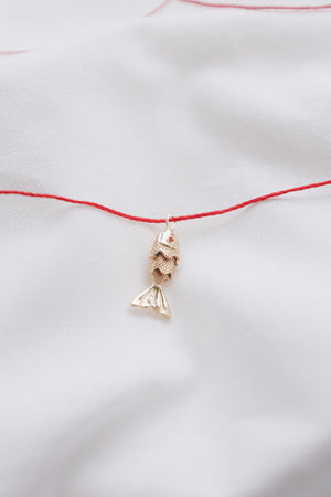 Gold fish pendant on a red string necklace, symbolizing luck and abundance.