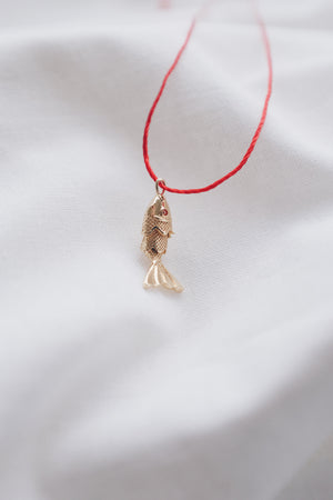 Gold fish pendant on a red string necklace, symbolizing luck and abundance.