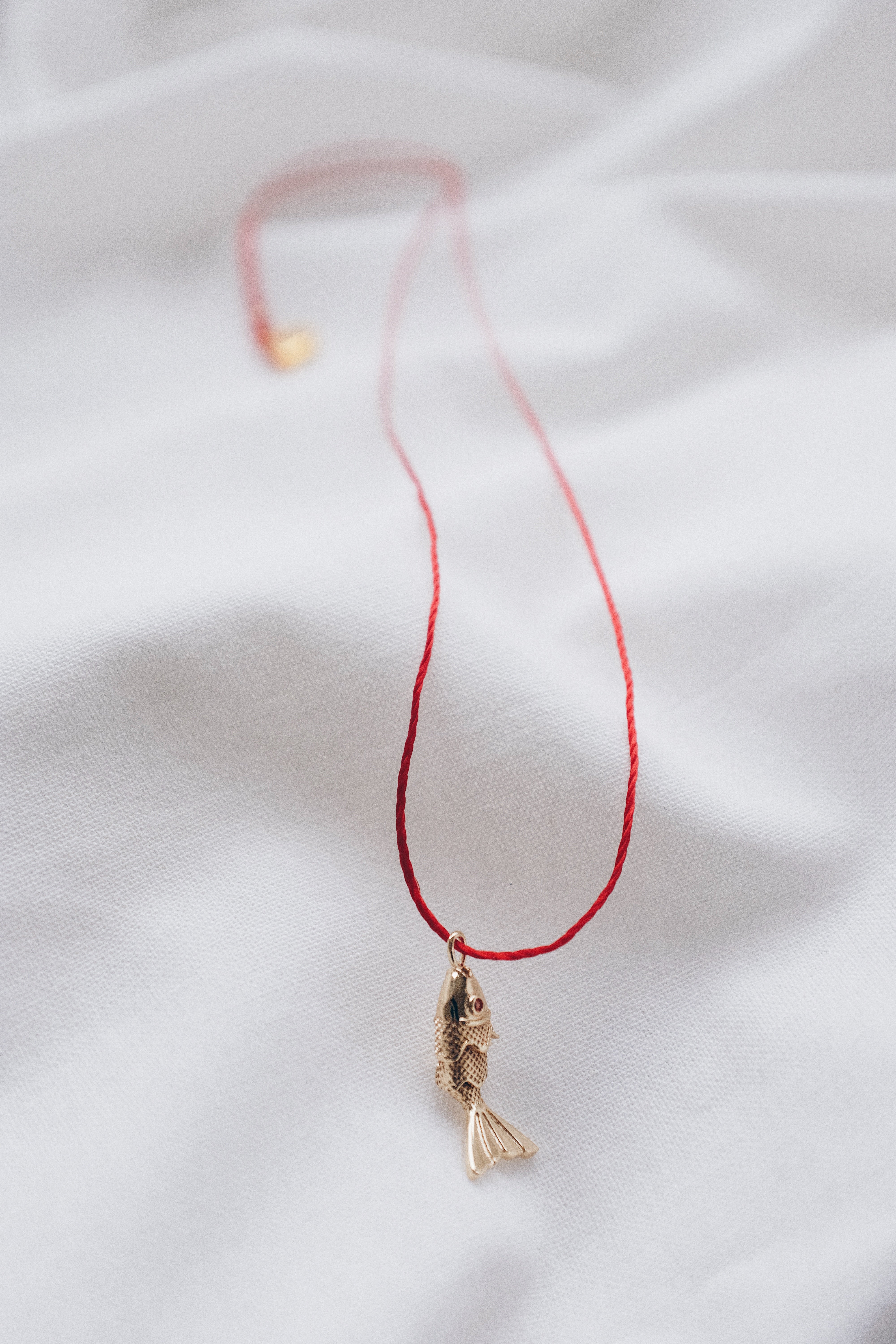 Gold fish pendant on a red string necklace, symbolizing luck and abundance.