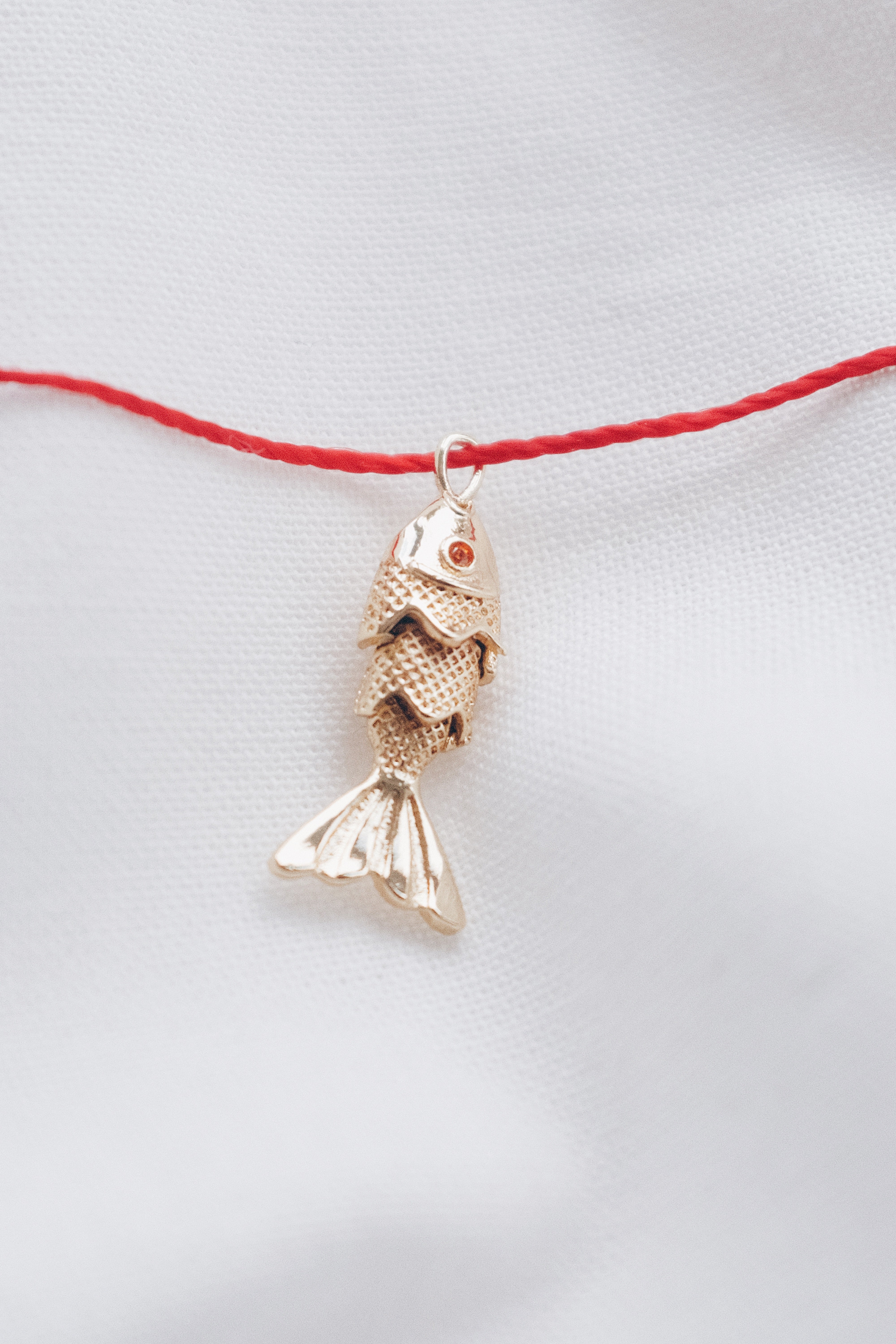 Gold fish pendant on a red string necklace, symbolizing luck and abundance.