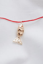 Gold fish pendant on a red string necklace, symbolizing luck and abundance.