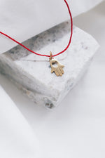 Gold hamsa hand pendant on red string necklace, symbolizing protection and blessings.