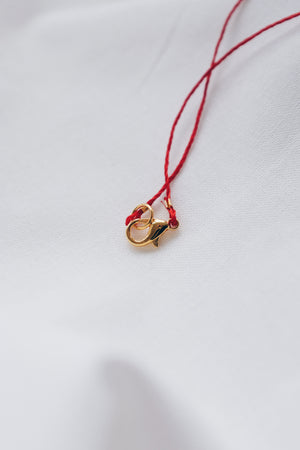 Gold tube pendant on a red string necklace, minimalist and stylish jewelry.