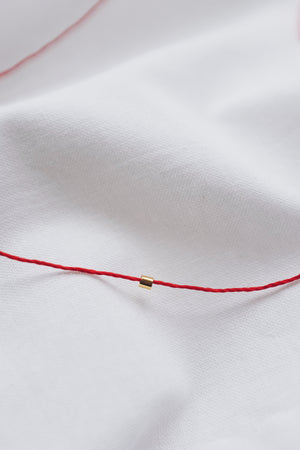 Gold tube pendant on a red string necklace, minimalist and stylish jewelry.