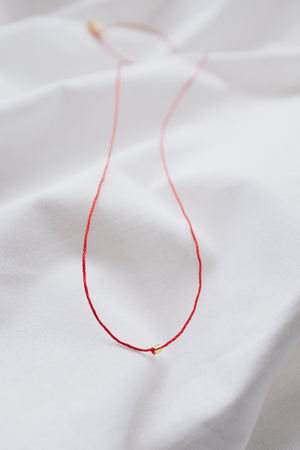 Gold tube pendant on a red string necklace, minimalist and stylish jewelry.