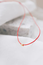 Gold tube pendant on a red string necklace, minimalist and stylish jewelry.