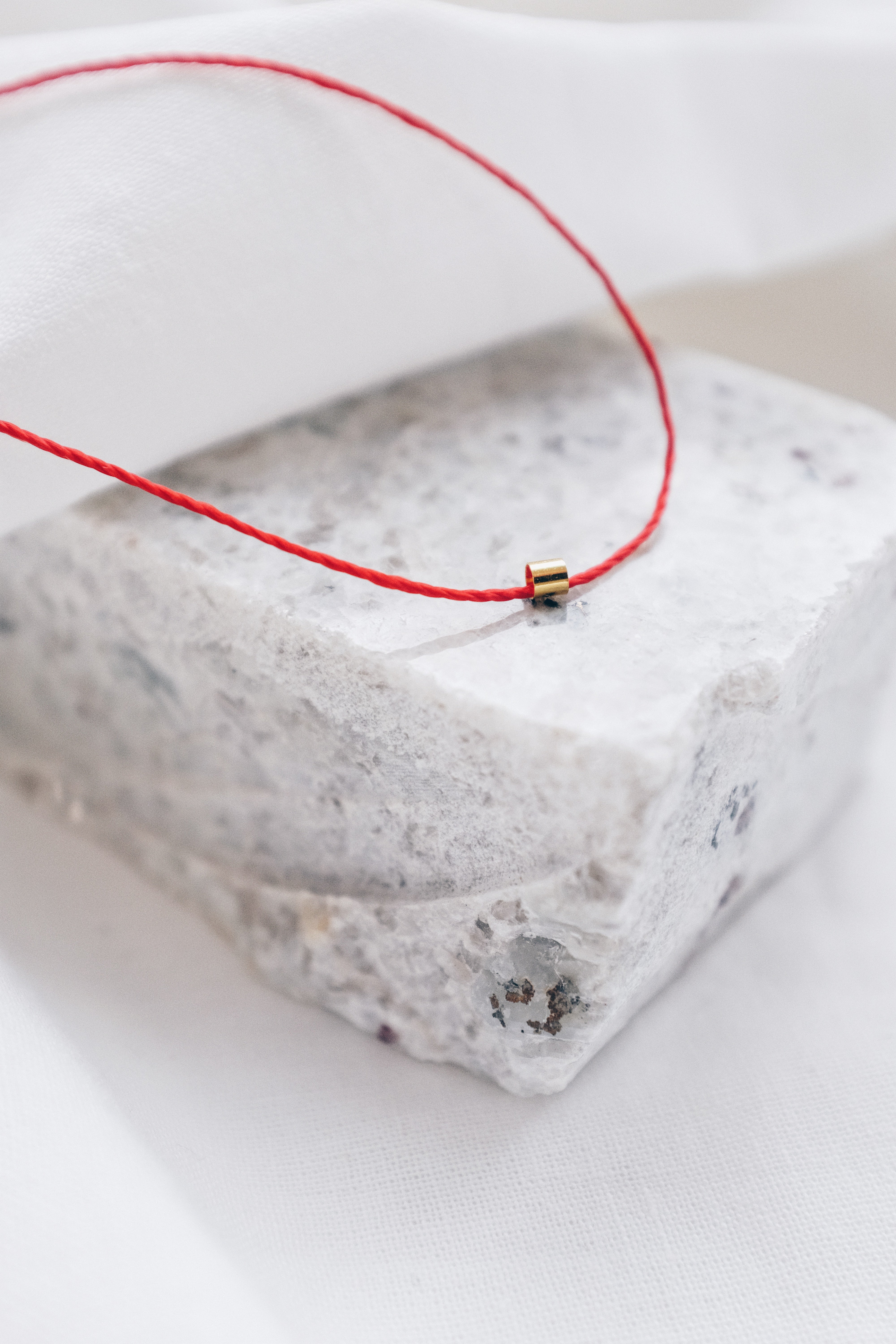 Gold tube pendant on a red string necklace, minimalist and stylish jewelry.