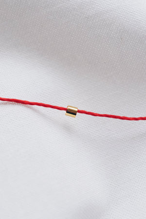 Gold tube pendant on a red string necklace, minimalist and stylish jewelry.