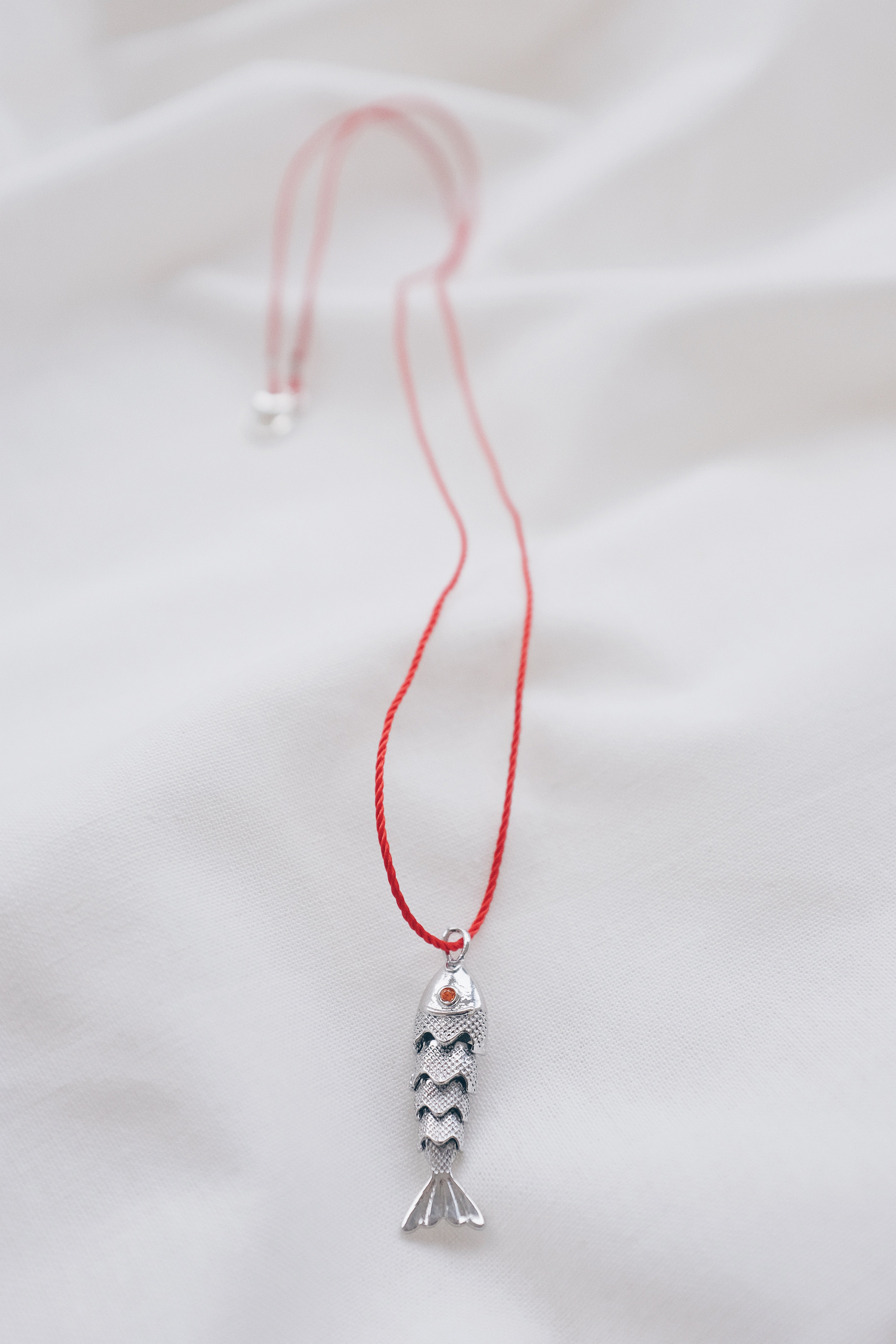 Silver fish pendant on a red string necklace, symbolizing luck and abundance.