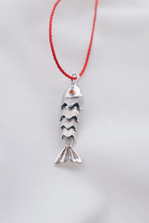 Silver fish pendant on a red string necklace, symbolizing luck and abundance.