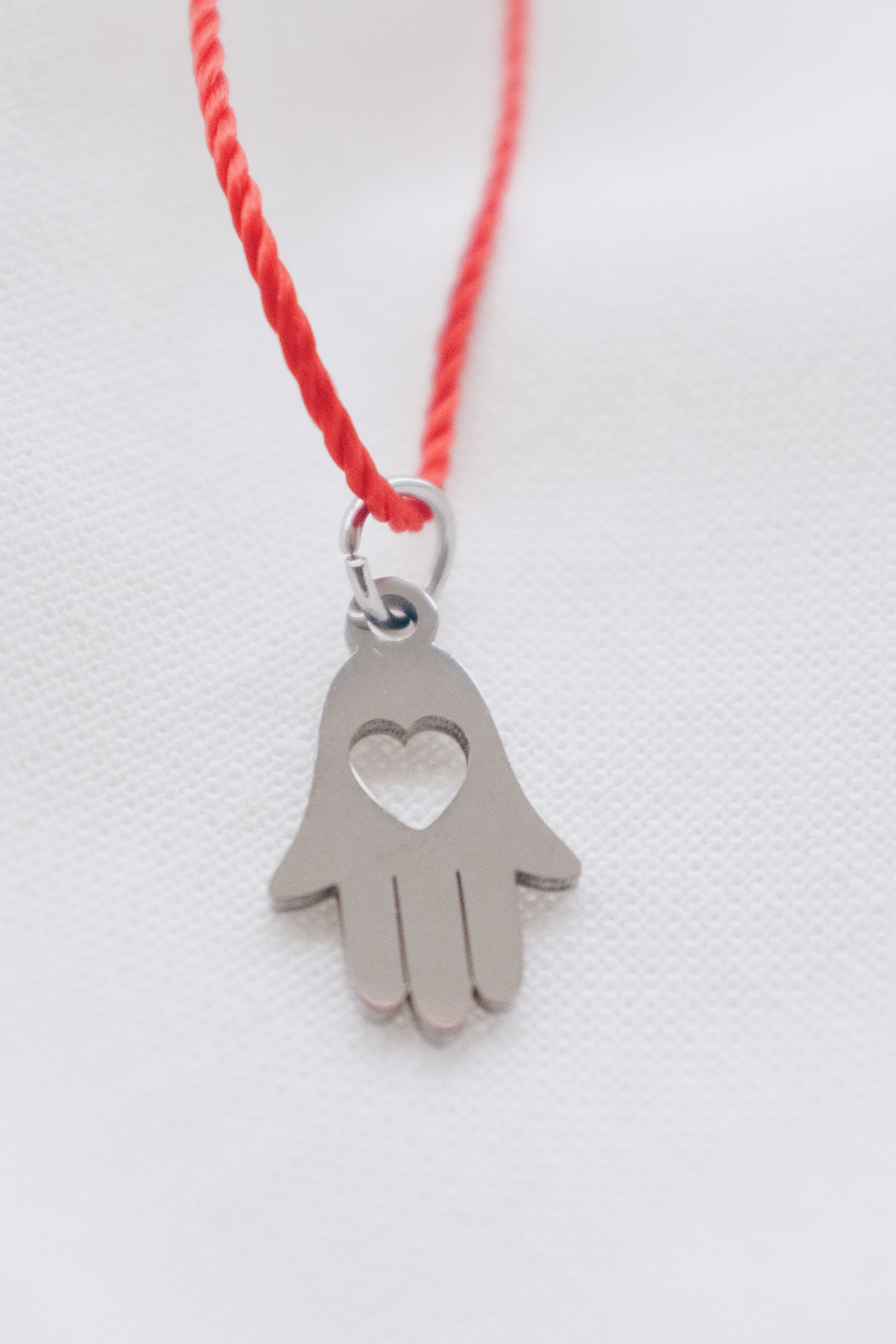 Silver hamsa hand pendant on red string necklace, symbolizing protection and blessings.