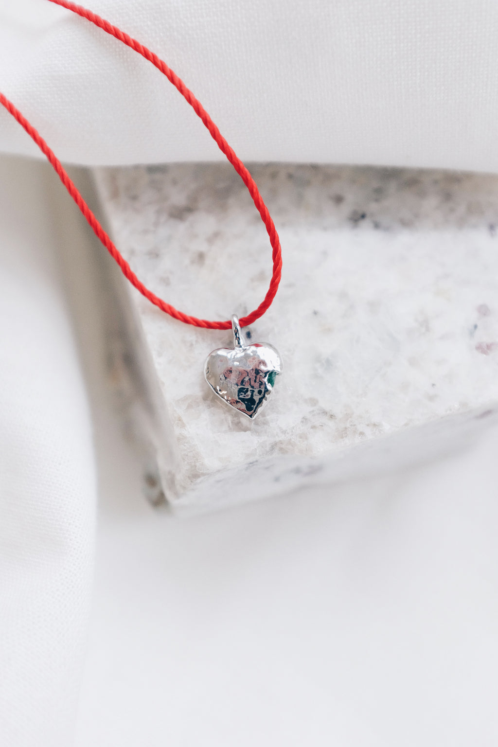 Silver heart pendant adorned with peridot gemstone on a red string necklace.