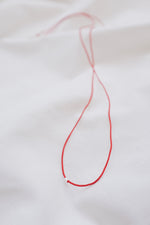 Silver tube pendant on a red string necklace, minimalist and stylish jewelry.